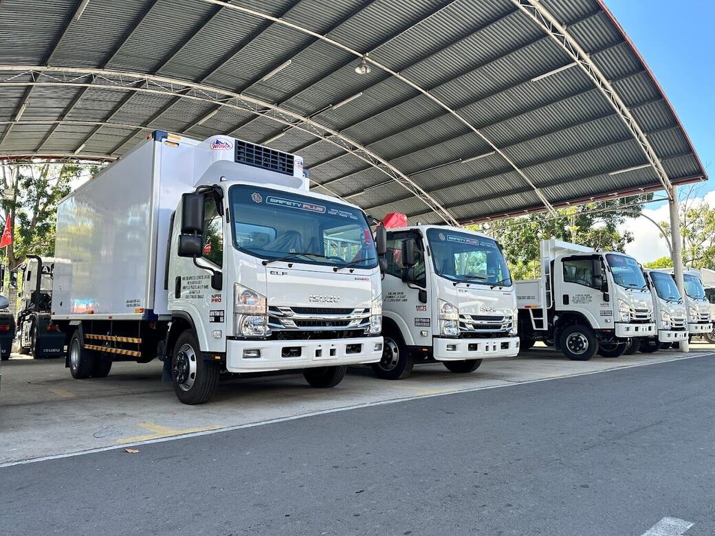 Row of new white refrigerated Isuzu trucks under a canopy